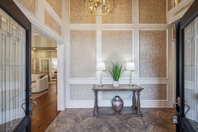 foyer entrance featuring wallpapered walls, a high ceiling, a chandelier, and a decorative wall