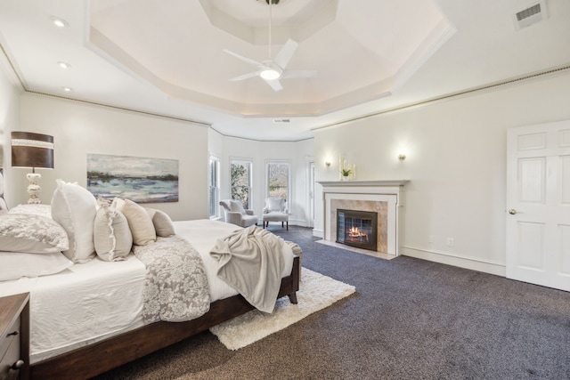 bedroom with a tray ceiling, dark colored carpet, visible vents, a tile fireplace, and baseboards