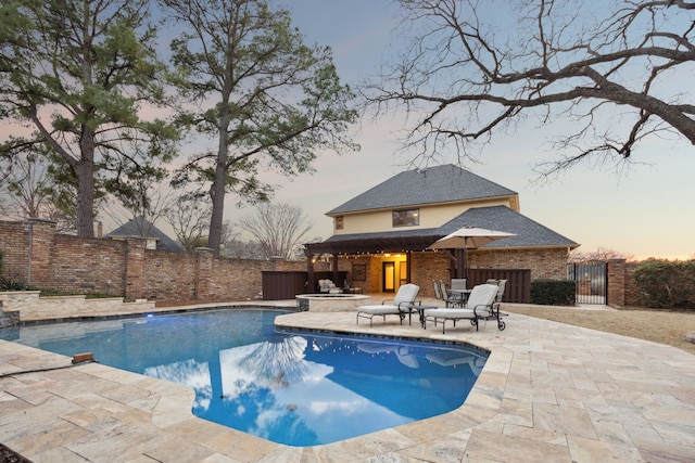 pool at dusk featuring an in ground hot tub, a patio area, a fenced backyard, and a fenced in pool