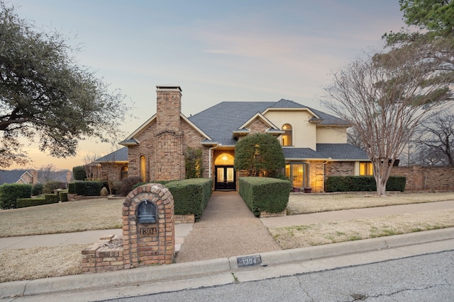 view of front of property featuring french doors, brick siding, a chimney, and roof with shingles