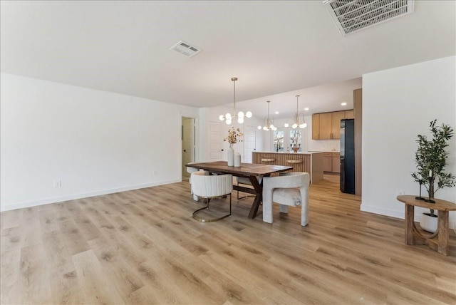 dining room featuring visible vents, light wood-style flooring, and an inviting chandelier