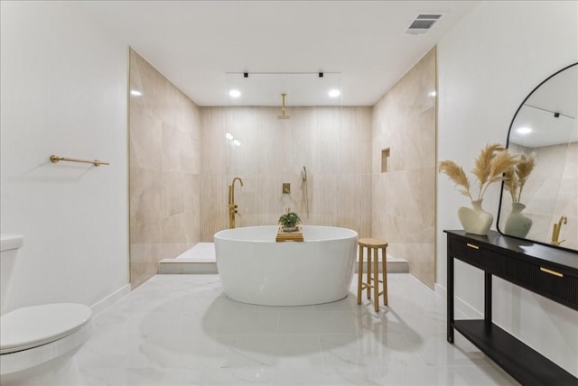 full bathroom with visible vents, toilet, marble finish floor, a freestanding tub, and tile walls