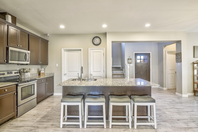 kitchen featuring a kitchen bar, light stone counters, stainless steel appliances, and a sink