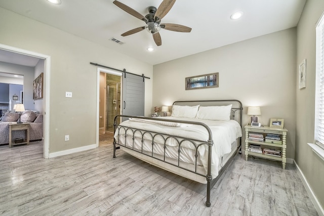 bedroom featuring wood finished floors, visible vents, baseboards, and a barn door