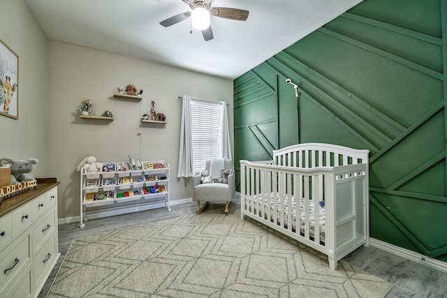 bedroom with a nursery area, ceiling fan, baseboards, and light wood finished floors