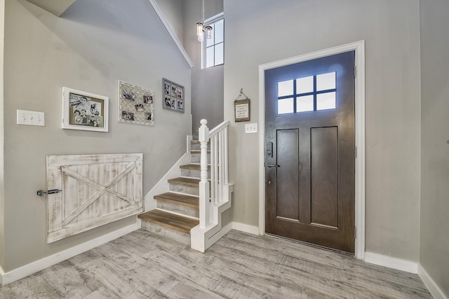 entryway featuring stairs, a towering ceiling, baseboards, and wood finished floors