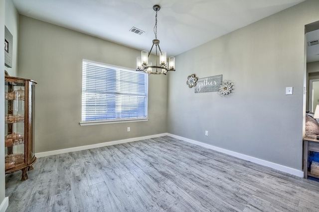 spare room with baseboards, visible vents, an inviting chandelier, and wood finished floors