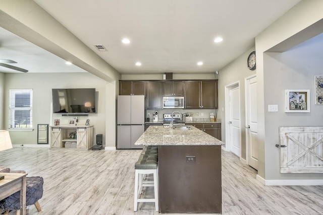 kitchen with visible vents, stainless steel microwave, light stone counters, dark brown cabinets, and fridge