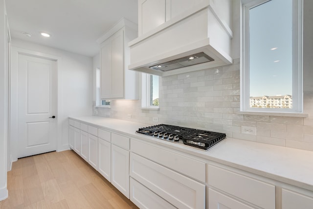 kitchen with stainless steel gas cooktop, white cabinetry, light countertops, backsplash, and custom exhaust hood