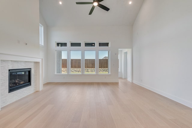 unfurnished living room with high vaulted ceiling, a glass covered fireplace, light wood-style floors, and baseboards