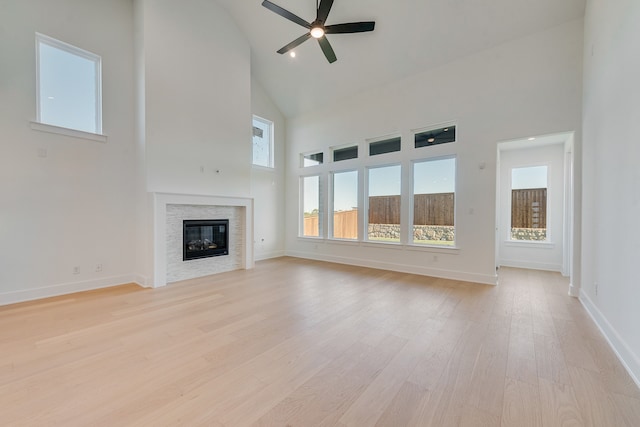 unfurnished living room featuring baseboards, high vaulted ceiling, a stone fireplace, and light wood-style floors