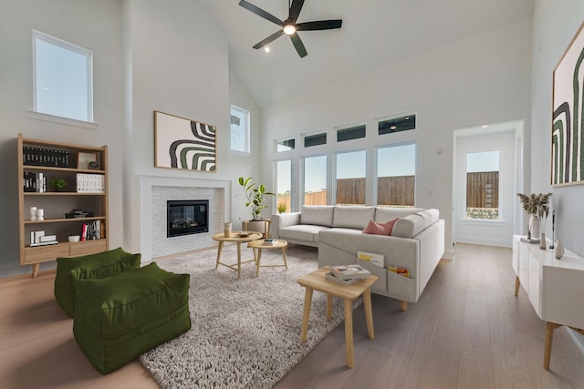 living area with a ceiling fan, high vaulted ceiling, wood finished floors, and a glass covered fireplace