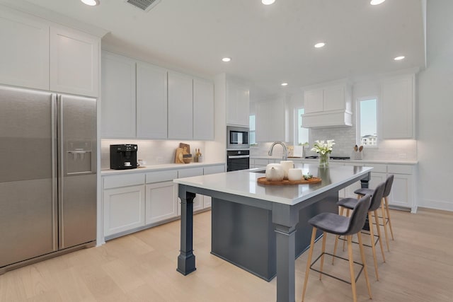 kitchen with stainless steel appliances, a kitchen breakfast bar, white cabinetry, and custom exhaust hood