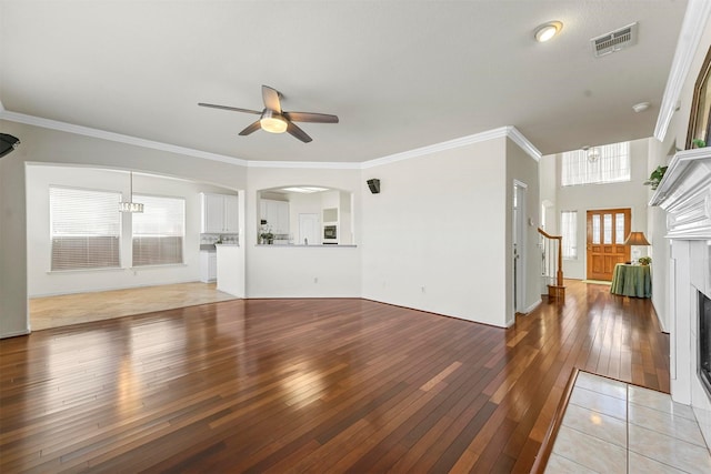 unfurnished living room with crown molding, visible vents, a fireplace with flush hearth, light wood-style floors, and ceiling fan