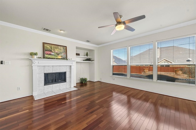 unfurnished living room with built in features, crown molding, visible vents, wood finished floors, and a tile fireplace