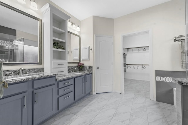 bathroom featuring marble finish floor, double vanity, a sink, and a walk in closet