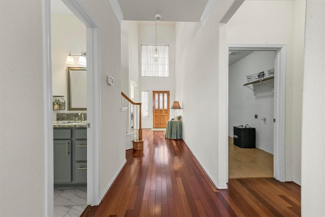 corridor with dark wood-style flooring, a sink, baseboards, and stairs