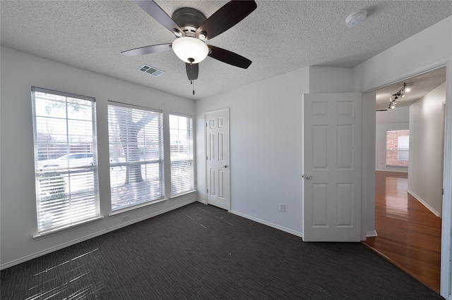 unfurnished room featuring a textured ceiling, dark carpet, visible vents, and a healthy amount of sunlight