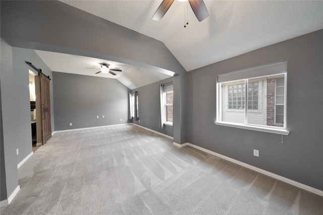 unfurnished living room with carpet floors, a barn door, vaulted ceiling, ceiling fan, and baseboards