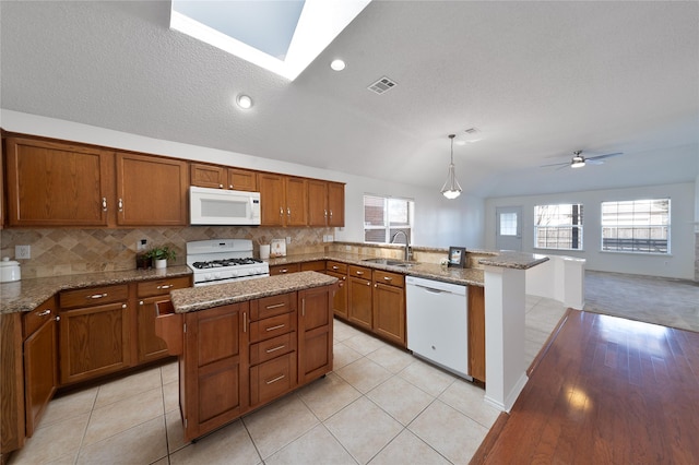 kitchen featuring white appliances, visible vents, brown cabinetry, a peninsula, and a sink