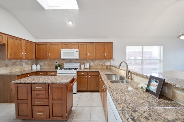 kitchen with white appliances, lofted ceiling with skylight, brown cabinets, and a sink