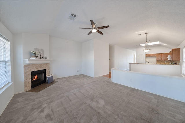 unfurnished living room featuring lofted ceiling, light colored carpet, a fireplace with flush hearth, a ceiling fan, and visible vents