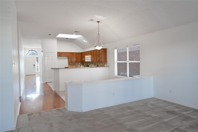 kitchen featuring lofted ceiling with skylight, a wealth of natural light, brown cabinets, and white microwave