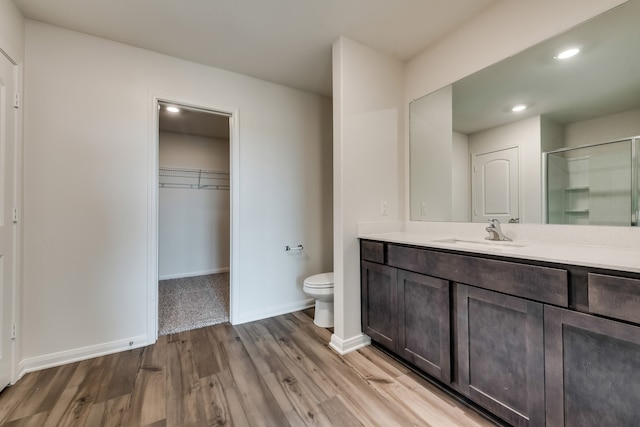 full bath featuring toilet, wood finished floors, vanity, baseboards, and a shower with door