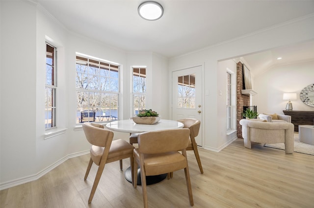 dining area featuring baseboards, light wood finished floors, a fireplace, and crown molding