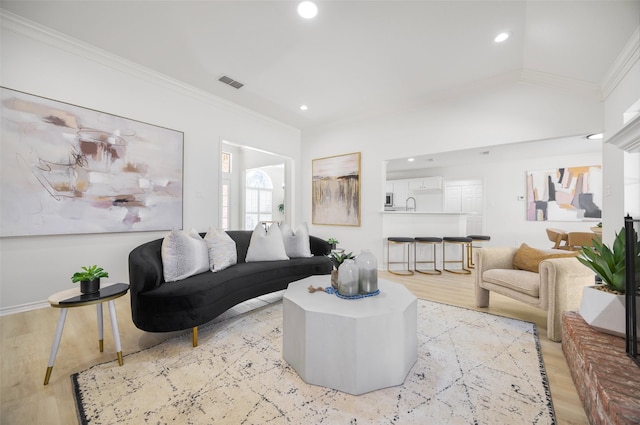 living area featuring visible vents, ornamental molding, vaulted ceiling, light wood-type flooring, and recessed lighting