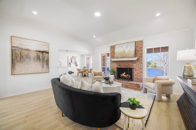 living area with baseboards, vaulted ceiling, crown molding, light wood-type flooring, and a fireplace