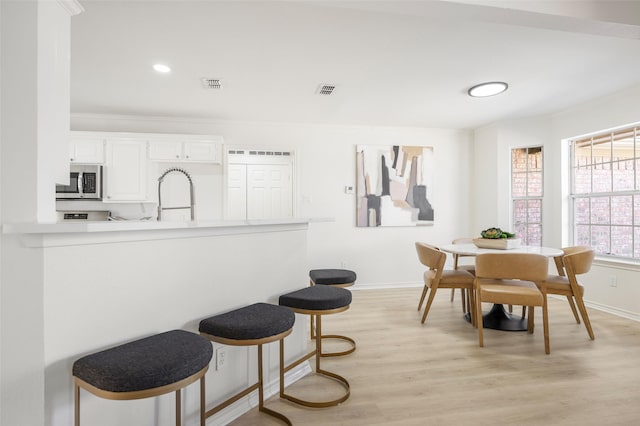 dining area featuring light wood-style flooring, recessed lighting, visible vents, baseboards, and ornamental molding