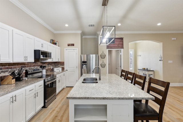 kitchen featuring arched walkways, stainless steel appliances, tasteful backsplash, a sink, and a kitchen bar