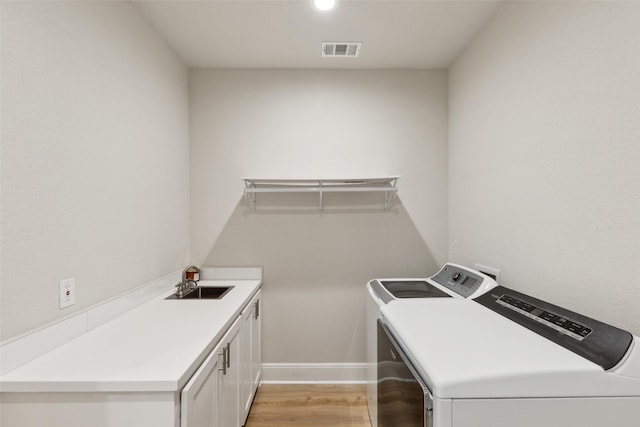 laundry room featuring a sink, visible vents, light wood-style floors, washer and dryer, and cabinet space