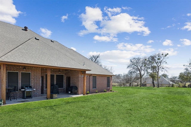 rear view of house with a yard, a shingled roof, a patio, and brick siding