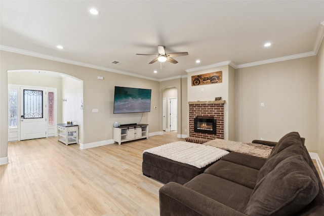 living room featuring arched walkways, baseboards, light wood-style floors, a brick fireplace, and crown molding