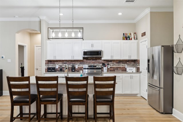 kitchen featuring arched walkways, stainless steel appliances, light wood finished floors, and white cabinetry