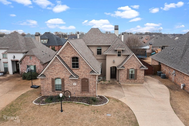 french country inspired facade featuring brick siding, a chimney, stucco siding, a shingled roof, and driveway