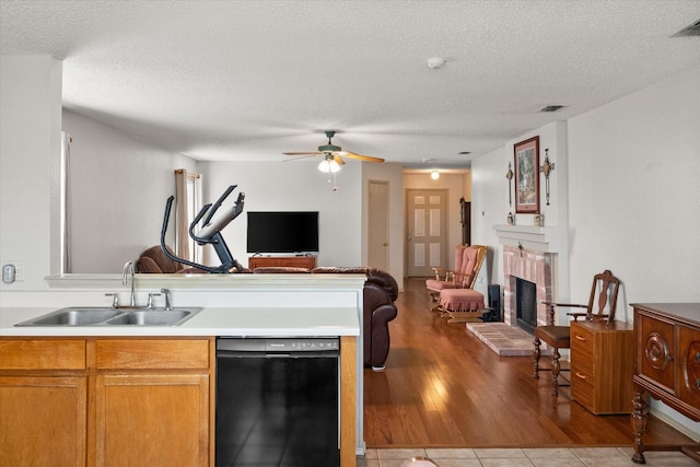 kitchen featuring dishwasher, open floor plan, light countertops, a brick fireplace, and a sink