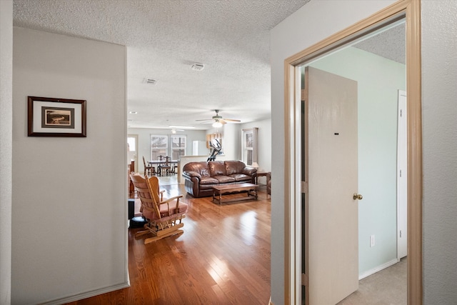 hall with light wood finished floors, baseboards, visible vents, and a textured ceiling