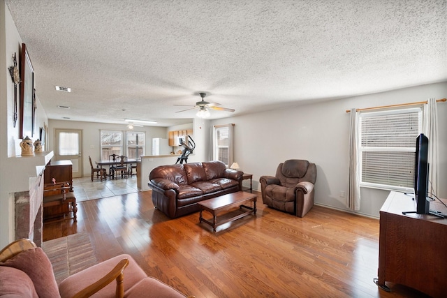 living room with visible vents, a ceiling fan, a textured ceiling, wood finished floors, and baseboards