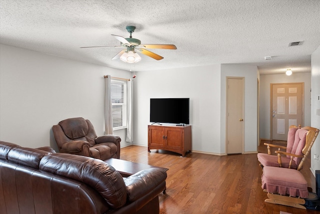 living room featuring visible vents, light wood-style flooring, ceiling fan, a textured ceiling, and baseboards