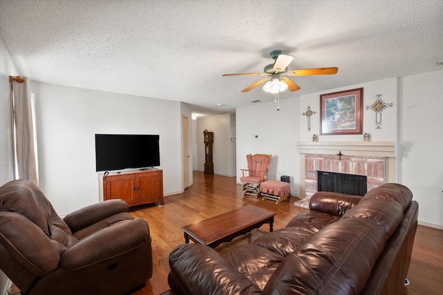 living room featuring light wood finished floors, a brick fireplace, a ceiling fan, and a textured ceiling