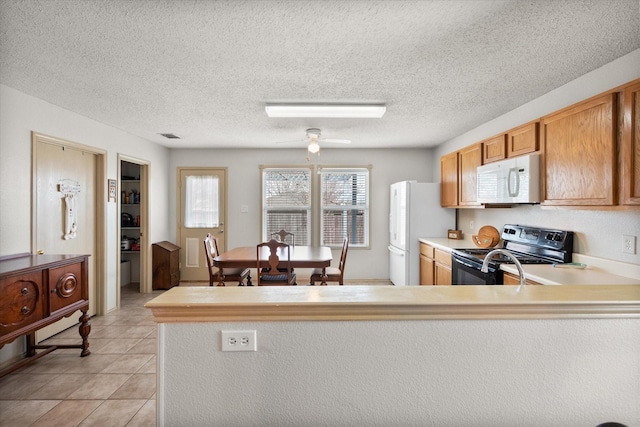 kitchen featuring light tile patterned floors, light countertops, a textured ceiling, white appliances, and a peninsula