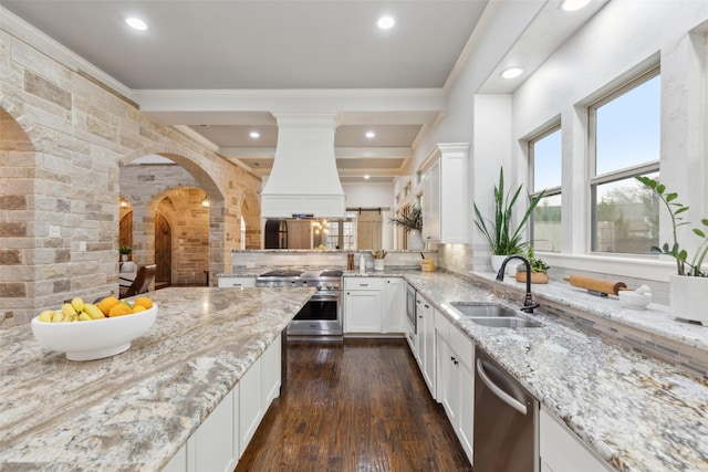 kitchen featuring arched walkways, a sink, appliances with stainless steel finishes, custom exhaust hood, and light stone countertops