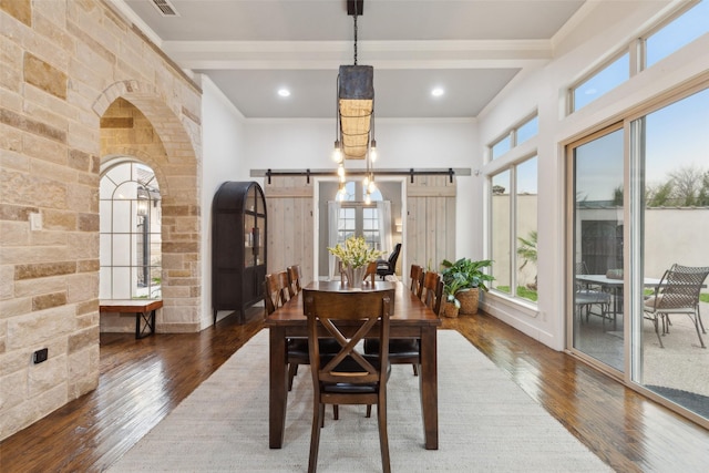 dining space with ornamental molding, a barn door, wood-type flooring, and arched walkways