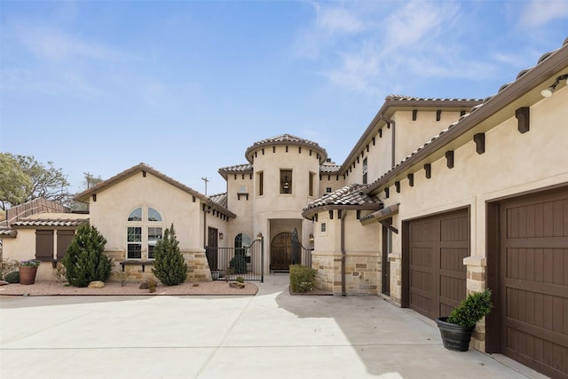 mediterranean / spanish home featuring driveway, stone siding, a tiled roof, a gate, and stucco siding