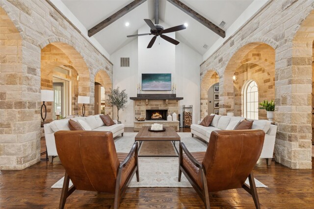 living room with visible vents, arched walkways, wood-type flooring, a stone fireplace, and high vaulted ceiling