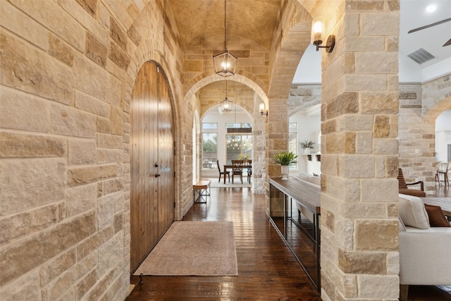 hall with arched walkways, hardwood / wood-style floors, vaulted ceiling, and visible vents