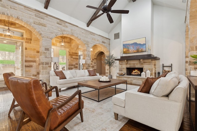 living room featuring visible vents, arched walkways, wood finished floors, beamed ceiling, and a stone fireplace